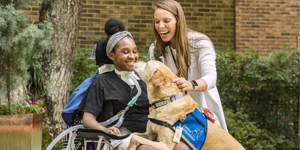 Canine Companions facility dog Barboza resting on lap of patient in wheelchair