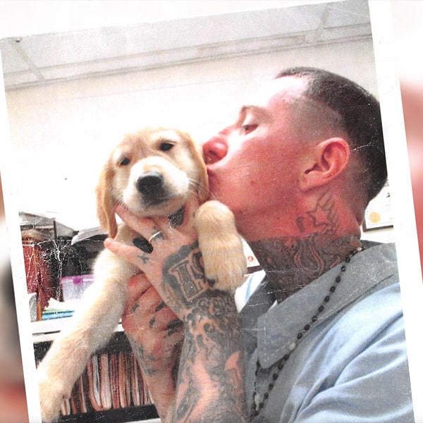 A man holds a young golden retriever puppy, kissing him on the head.