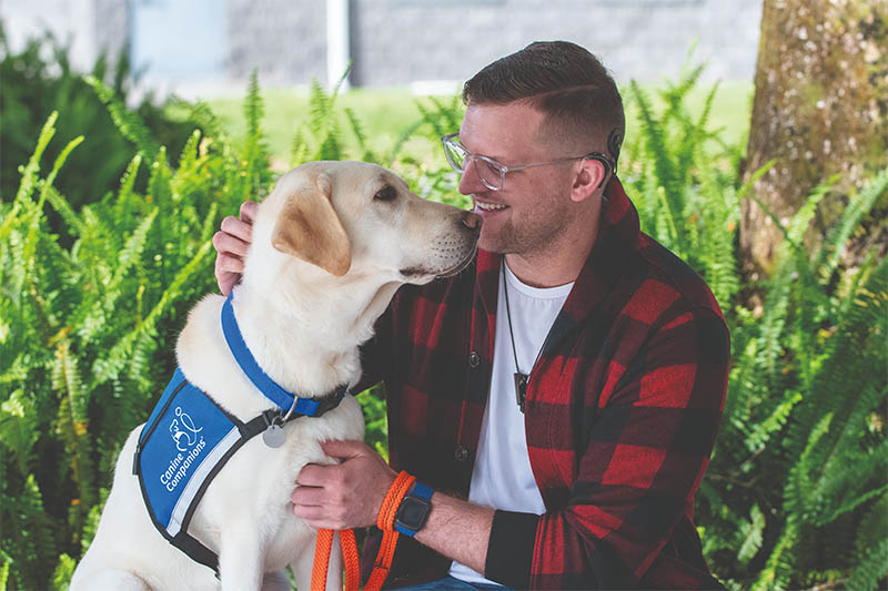 man and a Labrador sitting on a bench, with the man embracing the dog