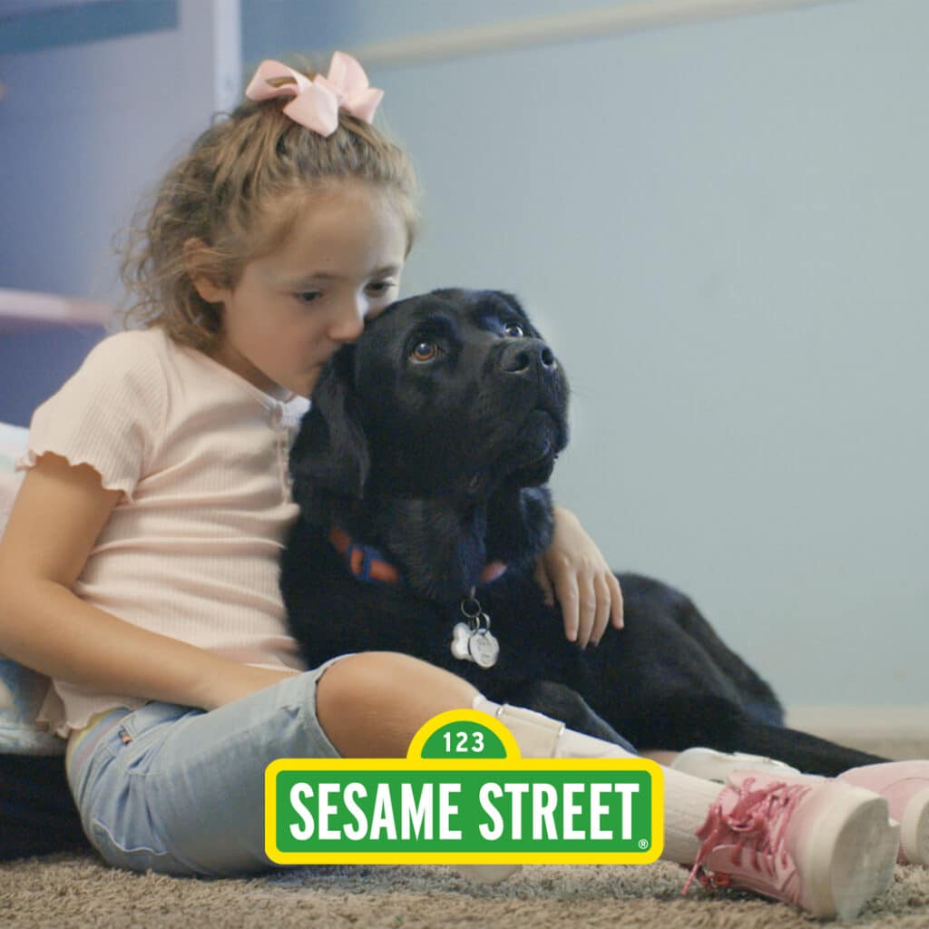 Young girl hugging and kissing her black lab service dog