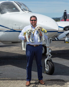 man holding canine companions puppies standing in front of a plane