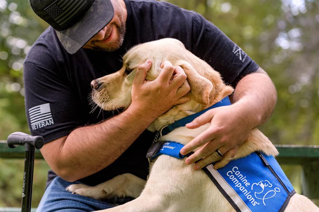 a man hugs his yellow lab service dog wearing a blue service dog vest