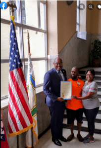 3 people holding a proclamation next to the US flag